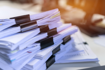Stacks of paper documents held together with binder clips, tinted deep navy.