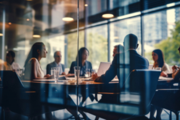 Executives around a boardroom table during a results meeting, viewed through a glass wall.